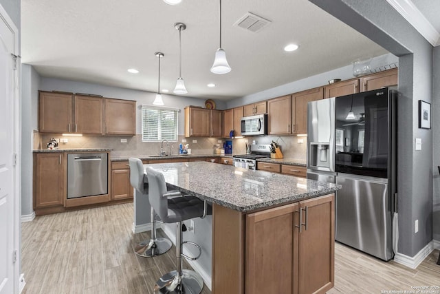 3402 Red Fls, San Antonio, TX 78253 - kitchen with stainless steel appliances, light wood-style flooring, a center island, brown cabinets, and stone counters