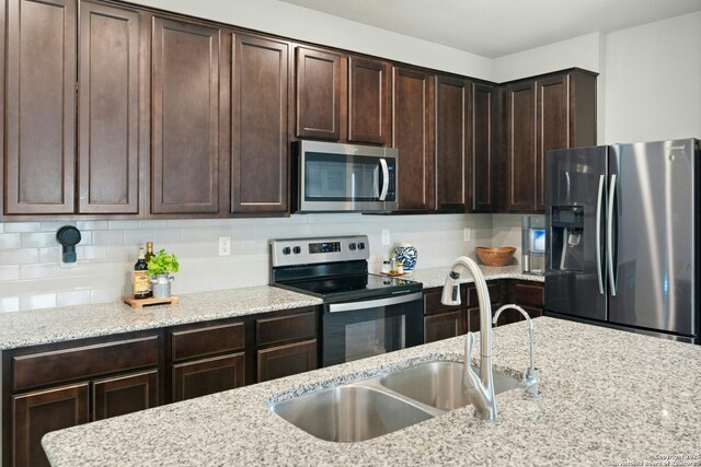 9210 Yaya Rd, Converse, TX 78109 - kitchen with appliances with stainless steel finishes, a sink, dark brown cabinets, light stone counters, and backsplash