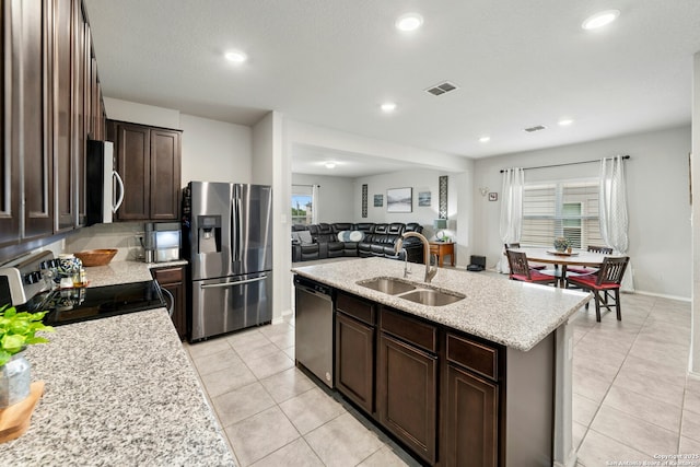 9210 Yaya Rd, Converse, TX 78109 - kitchen with stainless steel appliances, a sink, light tile patterned floors, a center island with sink, and dark brown cabinets