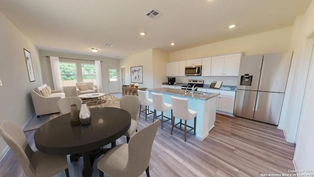 827 Goodhart, San Antonio, TX 78221 - kitchen featuring appliances with stainless steel finishes, white cabinets, an island with sink, light stone countertops, and light wood-style flooring