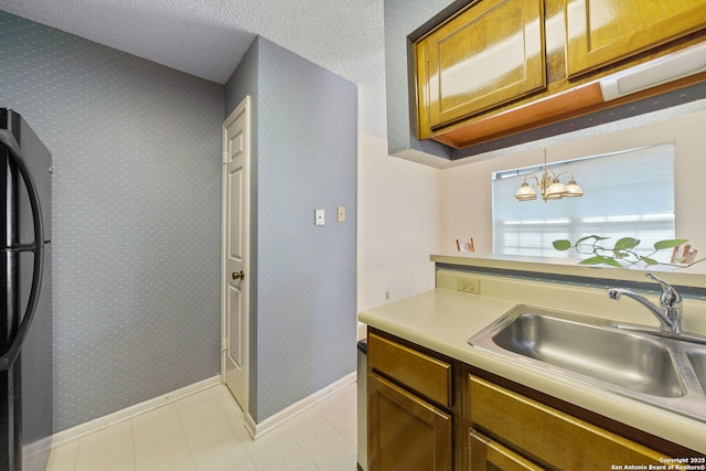 10955 Wurzbach Unit 905, San Antonio, TX 78230 - kitchen featuring freestanding refrigerator, a sink, light countertops, baseboards, and brown cabinetry
