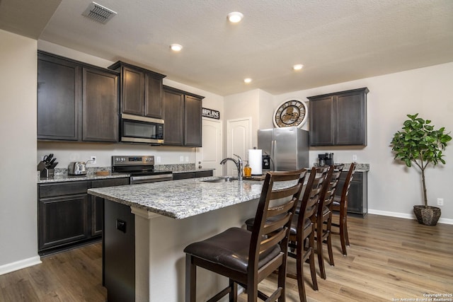 9123 Bennett Frst, Converse, TX 78109 - kitchen featuring appliances with stainless steel finishes, a sink, baseboards, wood finished floors, and a kitchen breakfast bar