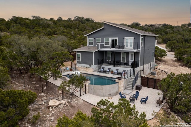 239 Damar Cv, Canyon Lake, TX 78133 - back of property at dusk with stairway, a balcony, a patio, an outdoor pool, and an in-ground hot tub