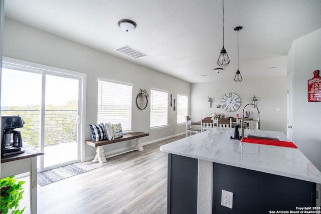 239 Damar Cv, Canyon Lake, TX 78133 - kitchen with hanging light fixtures, a sink, light stone countertops, light wood finished floors, and an island with sink