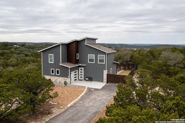 239 Damar Cv, Canyon Lake, TX 78133 - view of front of house with an attached garage, stone siding, asphalt driveway, board and batten siding, and a forest view