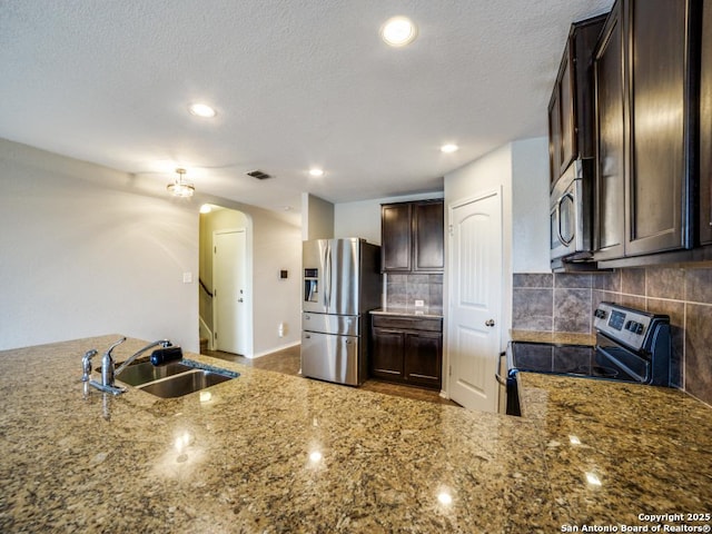 7010 Aphrodite Mist, San Antonio, TX 78252 - kitchen with appliances with stainless steel finishes, a sink, dark brown cabinets, tasteful backsplash, and arched walkways