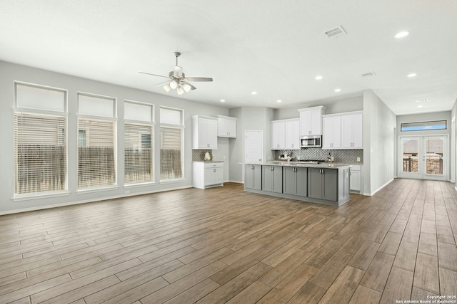 9304 Aggie Run, San Antonio, TX 78254 - kitchen with stainless steel microwave, open floor plan, white cabinets, wood finished floors, and an island with sink