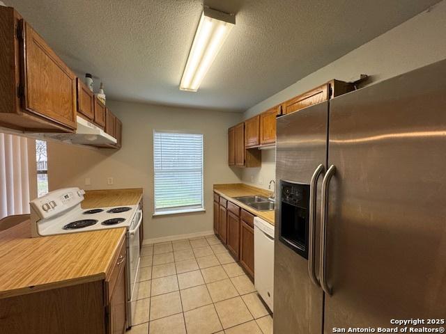 2854 Cherry Fld, San Antonio, TX 78245 - kitchen with white appliances, under cabinet range hood, light countertops, a textured ceiling, and a sink