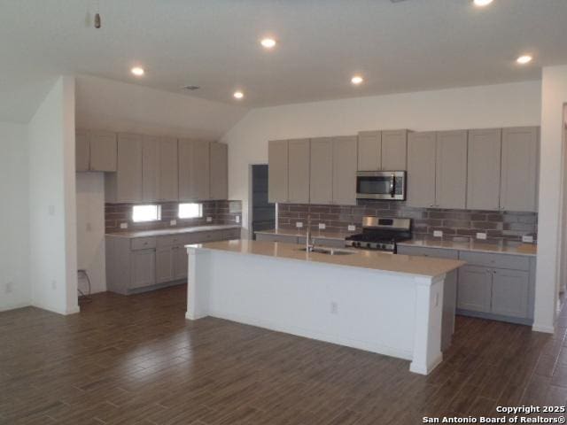 5919 Corsicana, Seguin, TX 78155 - kitchen featuring appliances with stainless steel finishes, decorative backsplash, a kitchen island with sink, dark wood finished floors, and a sink