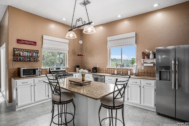 177 Ten W Dr, Comfort, TX 78013 - kitchen with stainless steel appliances, a textured wall, white cabinetry, stone counters, and a kitchen island
