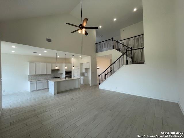12023 Horseshoe, San Antonio, TX 78254 - unfurnished living room with high vaulted ceiling, a ceiling fan, light wood-style flooring, recessed lighting, and stairs