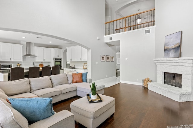 11227 Raw Sienna, Helotes, TX 78023 - living room featuring a towering ceiling, dark wood finished floors, baseboards, arched walkways, and a stone fireplace