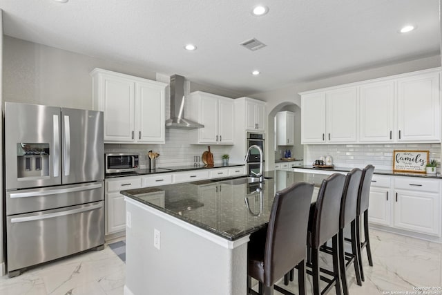 11227 Raw Sienna, Helotes, TX 78023 - kitchen featuring appliances with stainless steel finishes, wall chimney range hood, light marble finish floors, a sink, and arched walkways