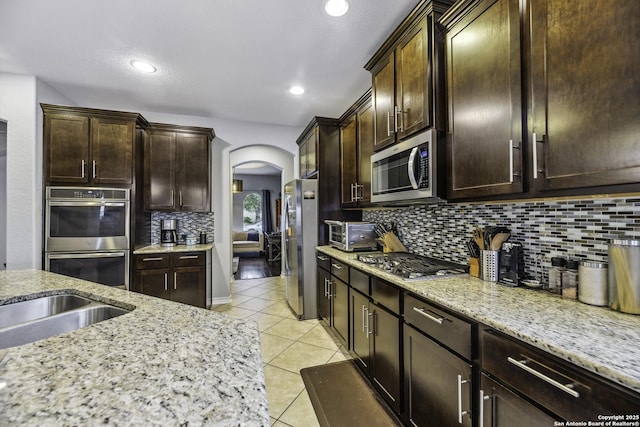 18131 Muir Glen Dr, San Antonio, TX 78257 - kitchen featuring appliances with stainless steel finishes, arched walkways, light tile patterned floors, backsplash, and dark brown cabinetry