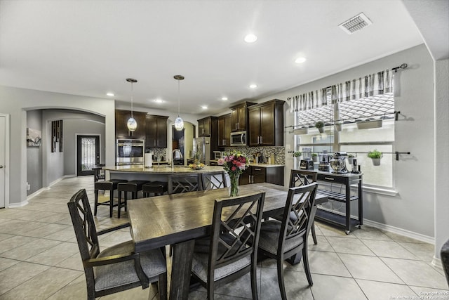 18131 Muir Glen Dr, San Antonio, TX 78257 - kitchen featuring stainless steel appliances, dark brown cabinets, arched walkways, light tile patterned flooring, and a kitchen island with sink