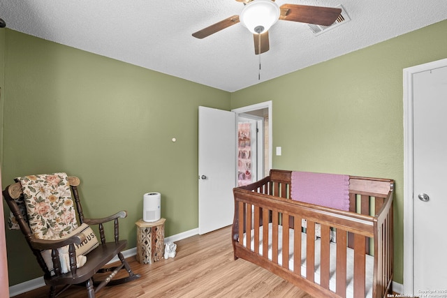 4303 Lakebend W, San Antonio, TX 78244 - bedroom featuring light wood-style flooring, a nursery area, baseboards, a textured ceiling, and ceiling fan