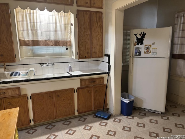 1927 Lee Hall, San Antonio, TX 78201 - kitchen featuring freestanding refrigerator, tile countertops, brown cabinets, and backsplash