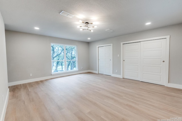 1071 Diamondhead Dr, Canyon Lake, TX 78133 - unfurnished bedroom with two closets, light wood-style flooring, a chandelier, baseboards, and a textured ceiling