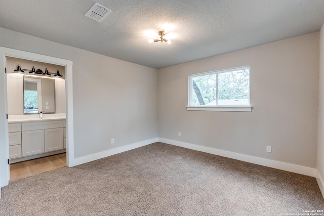 1071 Diamondhead Dr, Canyon Lake, TX 78133 - unfurnished bedroom featuring light carpet, baseboards, a sink, ensuite bath, and a textured ceiling