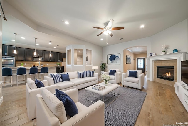 12827 Sabinal Riv, San Antonio, TX 78253 - living area featuring arched walkways, light wood-style floors, a ceiling fan, a tile fireplace, and recessed lighting