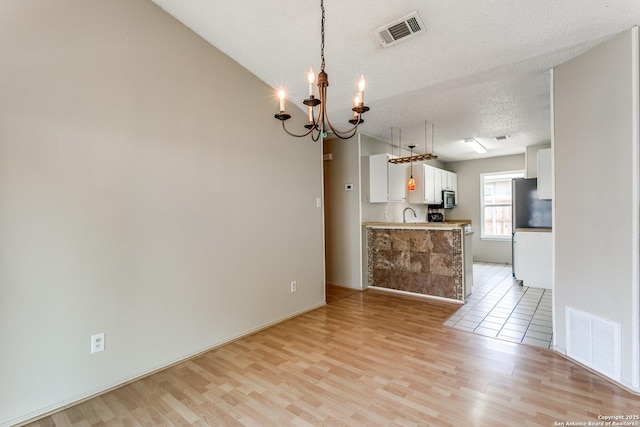 12215 Ridge Smt, San Antonio, TX 78247 - kitchen with stainless steel appliances, white cabinetry, light wood-style floors, a chandelier, and a textured ceiling