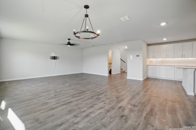 21902 Backspin, San Antonio, TX 78261 - unfurnished living room with light wood finished floors, a chandelier, stairway, baseboards, and recessed lighting