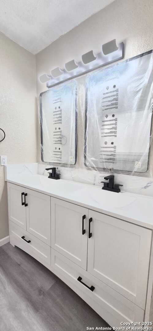 6115 Calderwood St, San Antonio, TX 78249 - bathroom featuring wood finished floors, double vanity, a textured ceiling, and baseboards