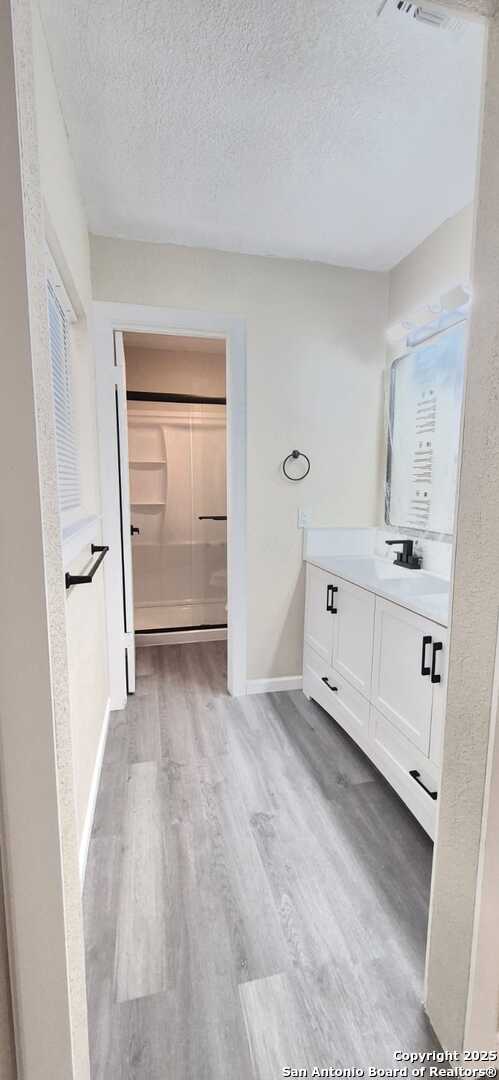 6115 Calderwood St, San Antonio, TX 78249 - full bathroom with vanity, wood finished floors, a textured ceiling, and baseboards