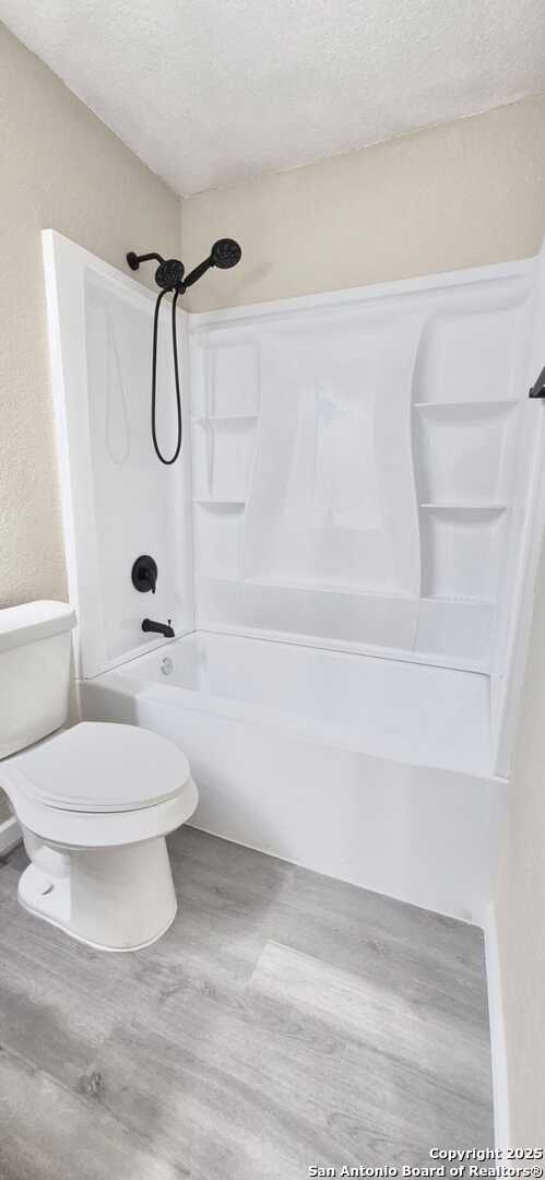 6115 Calderwood St, San Antonio, TX 78249 - full bathroom with toilet, wood finished floors, a textured ceiling, and shower / tub combination