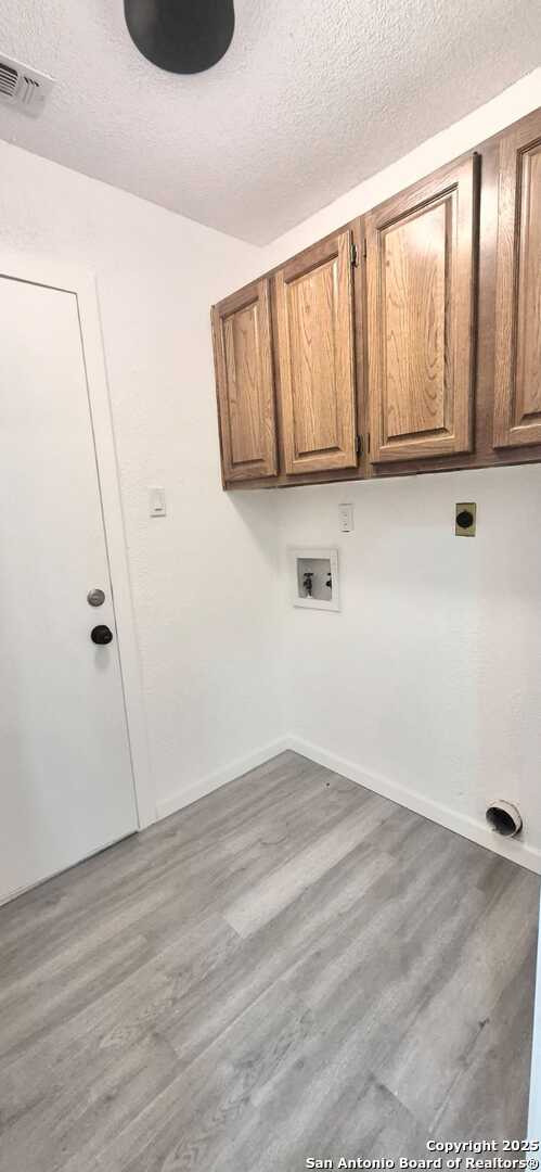 6115 Calderwood St, San Antonio, TX 78249 - laundry area with cabinet space, a textured ceiling, washer hookup, and wood finished floors