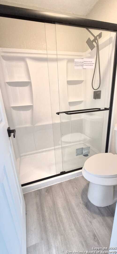 6115 Calderwood St, San Antonio, TX 78249 - full bath with wood finished floors, a shower stall, and toilet
