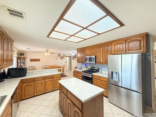 1185 County Road 7718, Devine, TX 78016 - kitchen featuring appliances with stainless steel finishes, light tile patterned floors, brown cabinets, light countertops, and a peninsula