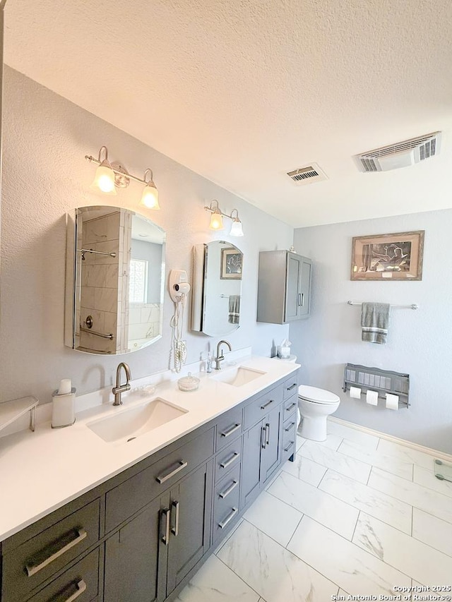 1185 County Road 7718, Devine, TX 78016 - full bath featuring a textured ceiling, double vanity, marble look tiles, tiled shower, and toilet