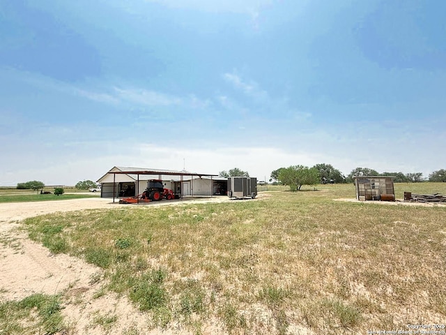 1185 County Road 7718, Devine, TX 78016 - view of green lawn with dirt driveway, a carport, a rural view, and an outbuilding