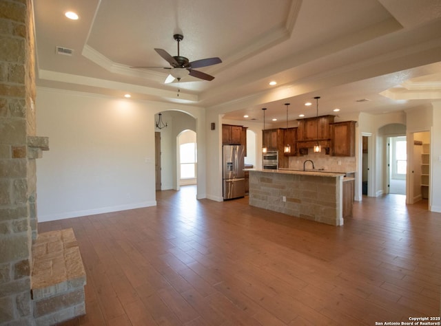2516 County Road 357, La Vernia, TX 78121 - unfurnished living room featuring a tray ceiling, arched walkways, ceiling fan, a sink, and baseboards