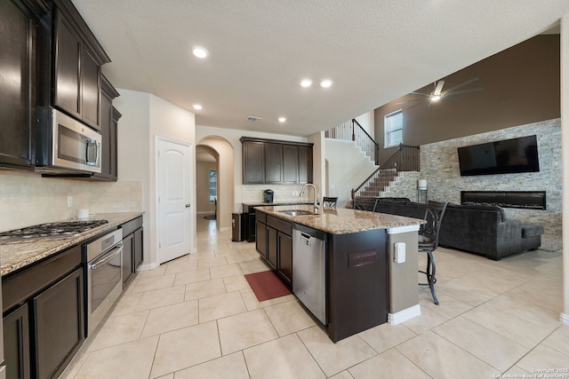 8726 Hideout, San Antonio, TX 78254 - kitchen featuring stainless steel appliances, arched walkways, light stone counters, a ceiling fan, and decorative backsplash
