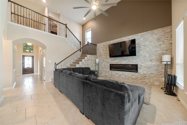 8726 Hideout, San Antonio, TX 78254 - tiled living area with arched walkways, a towering ceiling, a ceiling fan, a stone fireplace, and baseboards
