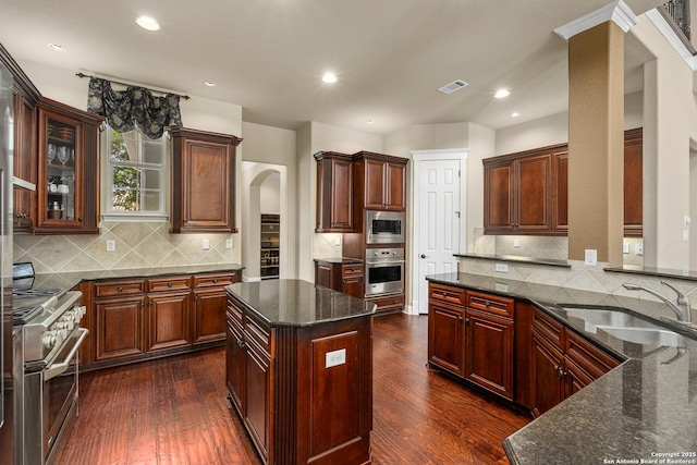 7414 Hovingham, San Antonio, TX 78257 - kitchen with appliances with stainless steel finishes, arched walkways, dark wood finished floors, a sink, and dark stone counters