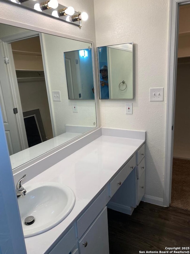 1336 Churing, San Antonio, TX 78245 - bathroom featuring vanity, wood finished floors, a walk in closet, baseboards, and a textured wall