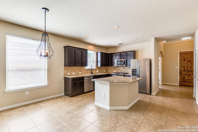 27511 Smokey Chase, Boerne, TX 78015 - kitchen featuring appliances with stainless steel finishes, decorative backsplash, dark brown cabinetry, a center island, and light stone counters