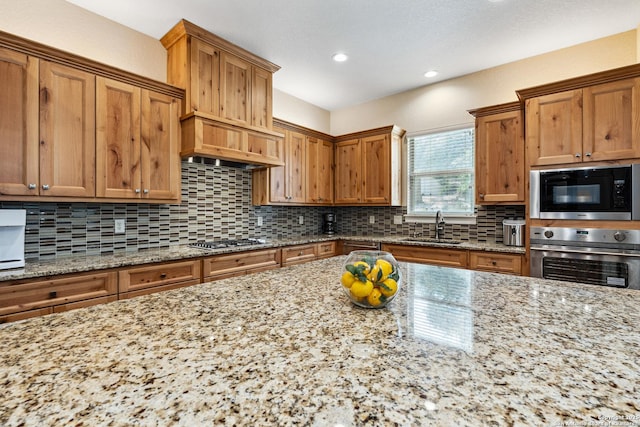 1015 Broken Spoke, Canyon Lake, TX 78133 - kitchen featuring appliances with stainless steel finishes, a sink, light stone countertops, tasteful backsplash, and brown cabinets