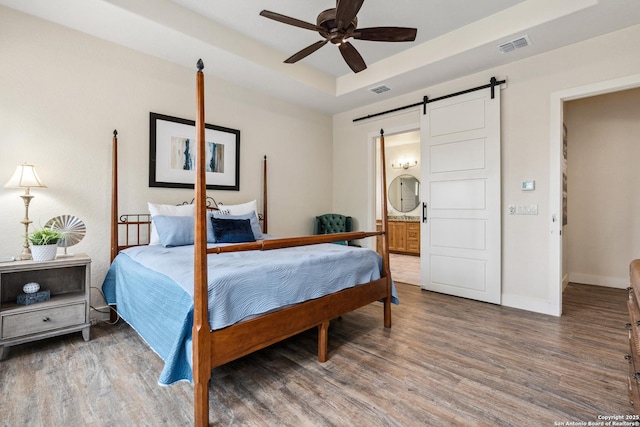 1015 Broken Spoke, Canyon Lake, TX 78133 - bedroom featuring a barn door, a raised ceiling, wood finished floors, connected bathroom, and baseboards