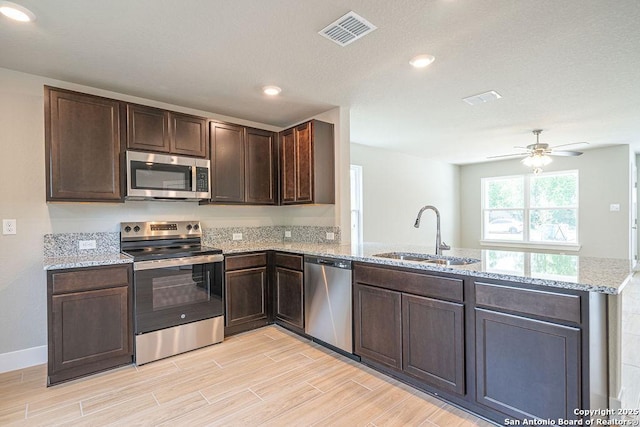 324 Mar Hl, Seguin, TX 78155 - kitchen featuring appliances with stainless steel finishes, a sink, a peninsula, dark brown cabinets, and light wood-type flooring