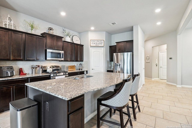 2730 Tortuga Verde, San Antonio, TX 78245 - kitchen featuring stainless steel appliances, an island with sink, light stone countertops, a breakfast bar, and dark brown cabinets