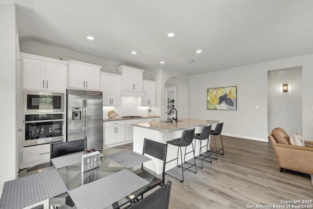 562 Orchard Way, New Braunfels, TX 78132 - kitchen featuring stainless steel appliances, arched walkways, a kitchen island with sink, light wood-style floors, and white cabinets