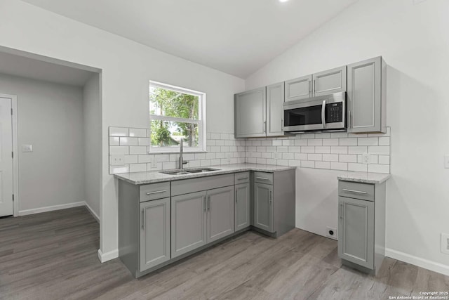 1711 Hermine, San Antonio, TX 78201 - kitchen with stainless steel microwave, gray cabinets, a sink, vaulted ceiling, and light wood-style floors