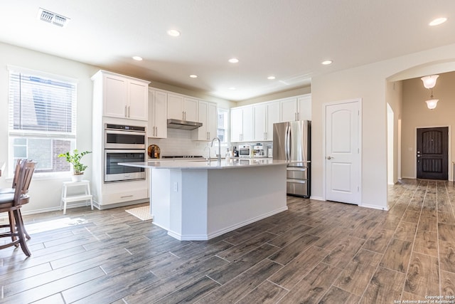 7421 Cimarron Lk, Boerne, TX 78015 - kitchen with appliances with stainless steel finishes, under cabinet range hood, arched walkways, dark wood-style flooring, and light countertops