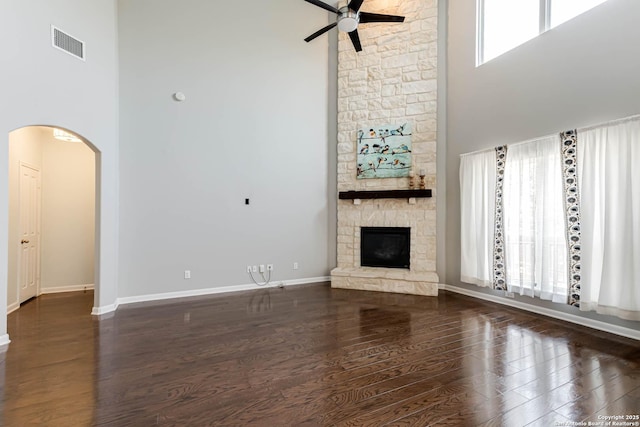 3319 Brooktree Ct, San Antonio, TX 78261 - unfurnished living room featuring a towering ceiling, a ceiling fan, arched walkways, a stone fireplace, and wood finished floors