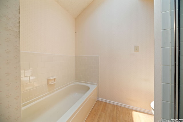 11334 Bald Mountain Dr, San Antonio, TX 78245 - full bathroom with wood finished floors, wallpapered walls, a bath, vaulted ceiling, and baseboards