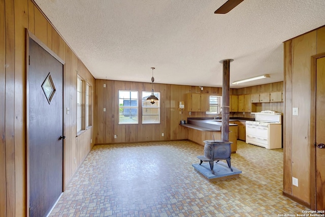 1212 County Road 337, La Vernia, TX 78121 - kitchen featuring a wood stove, white range with gas cooktop, wooden walls, a peninsula, and a textured ceiling